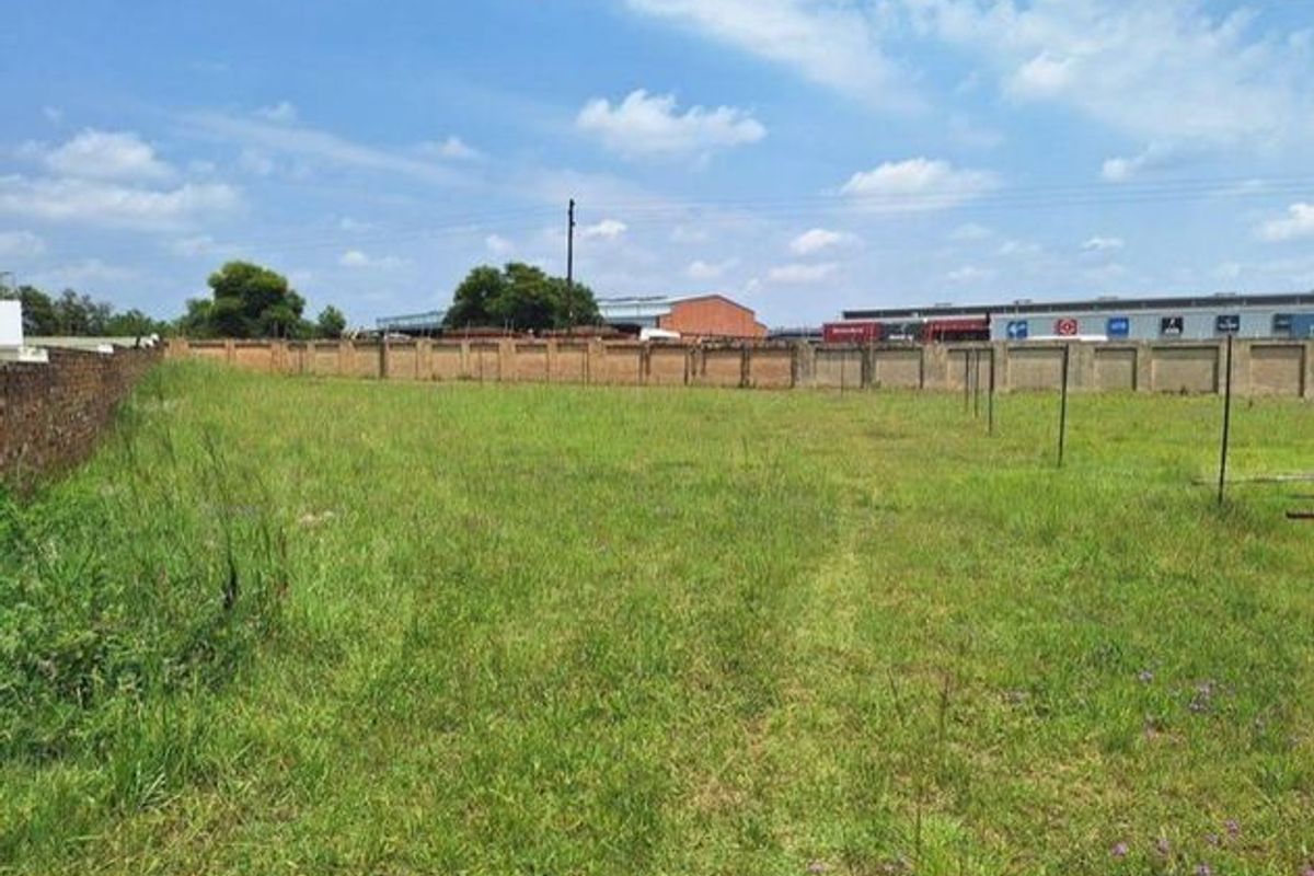 A vacant residential plot of land featuring grass coverage and a perimeter boundary wall.