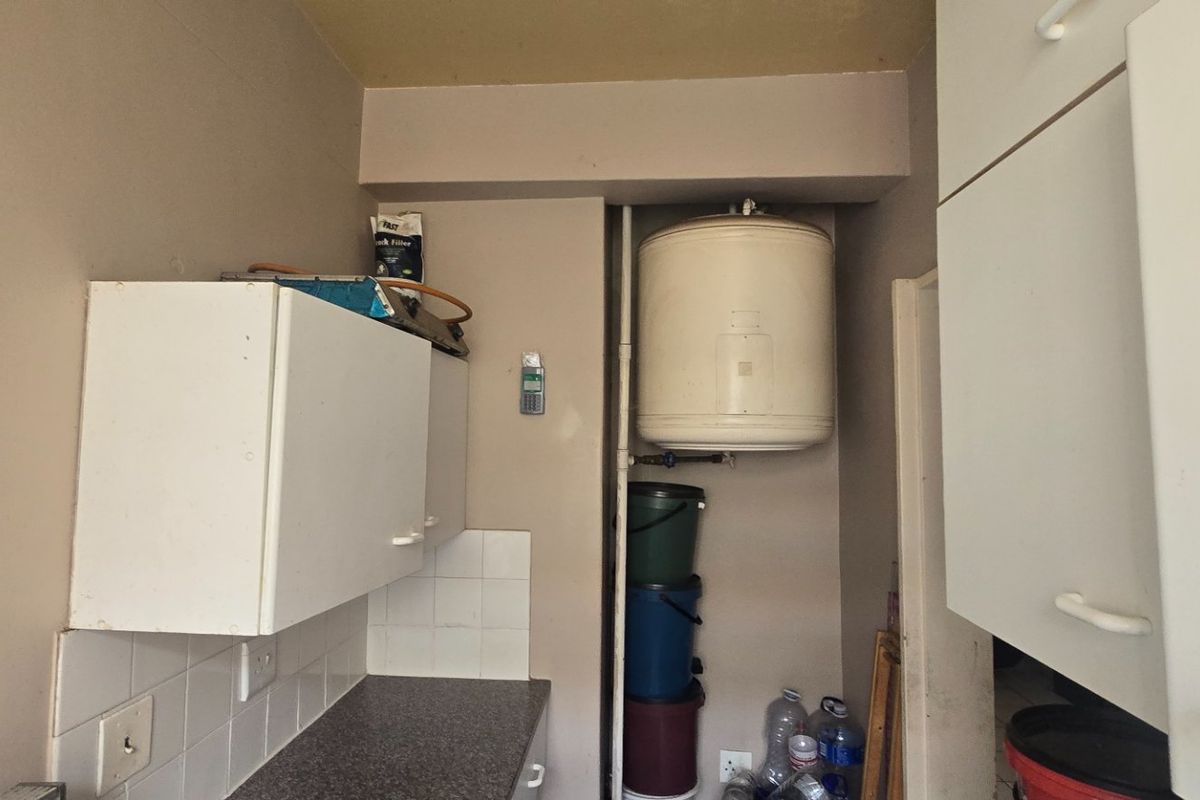 A functional scullery area featuring built-in cabinetry, laminate countertops, tiled splashbacks, and a wall-mounted electric water heater.