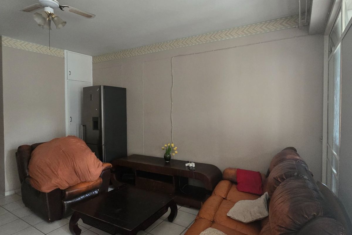A living room featuring tiled flooring, a ceiling fan, and a built-in cupboard, with neutral wall tones and visible surface-mounted electrical wiring.