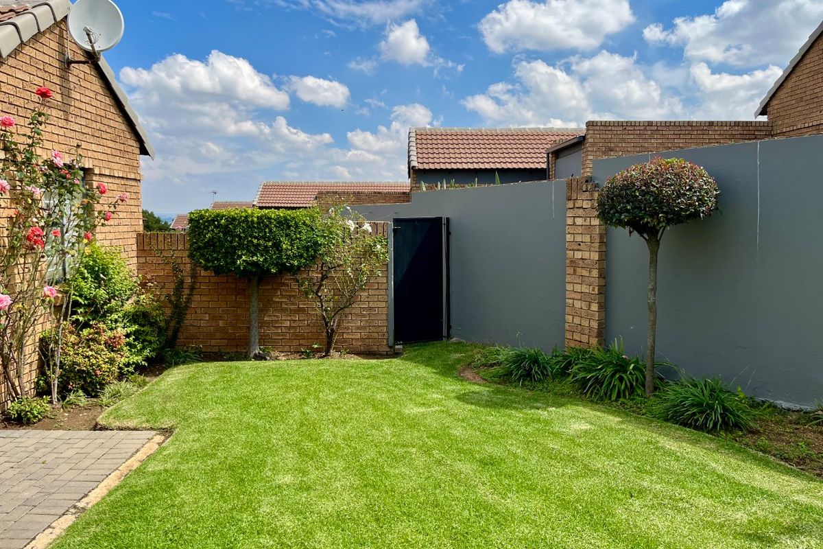 A well-maintained private rear garden featuring a manicured lawn, paved patio area, and secure perimeter walling with a side access gate.