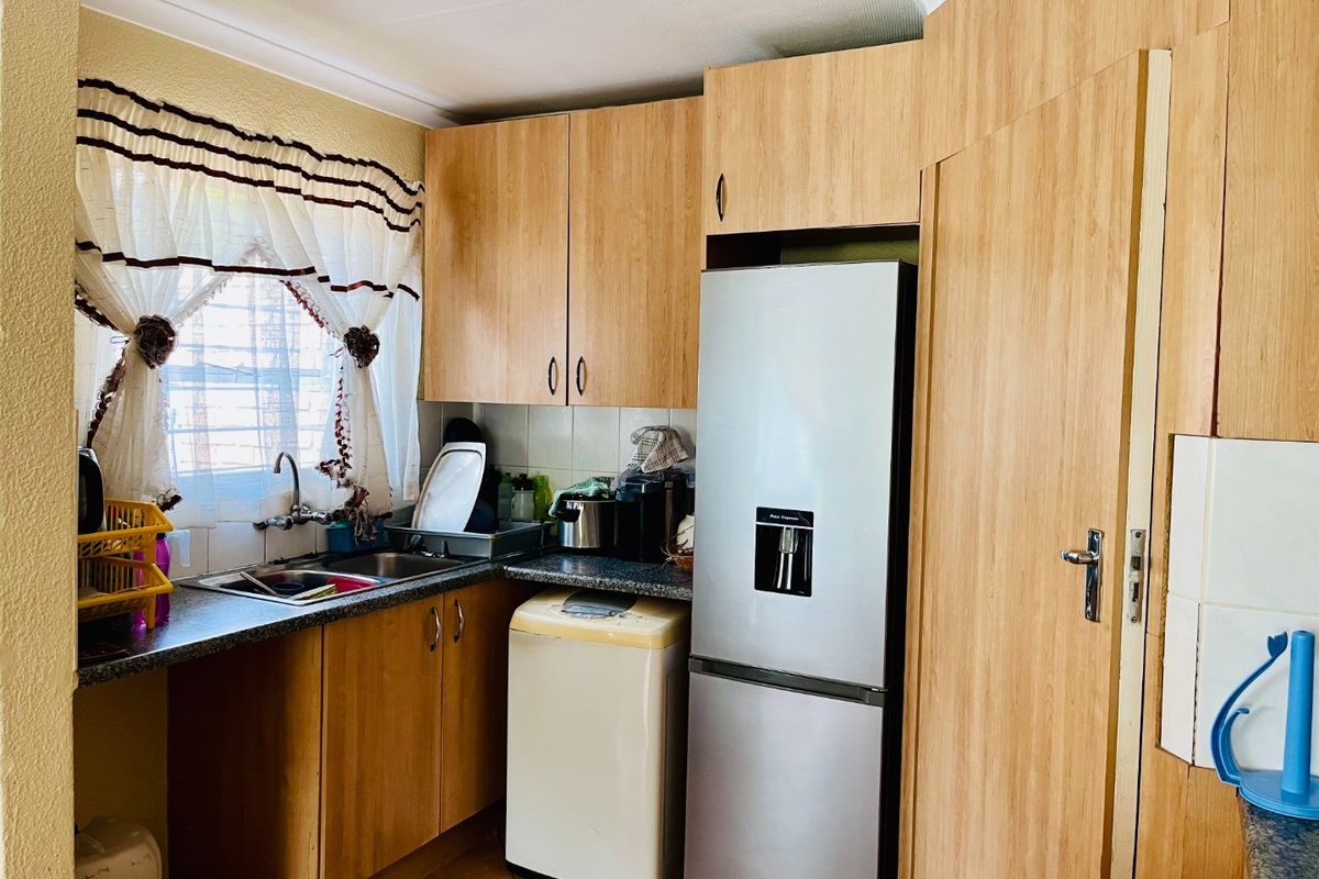 A functional kitchen featuring laminate cabinetry, dark countertops, a stainless steel sink, and tiled flooring, offering a practical layout for daily use.