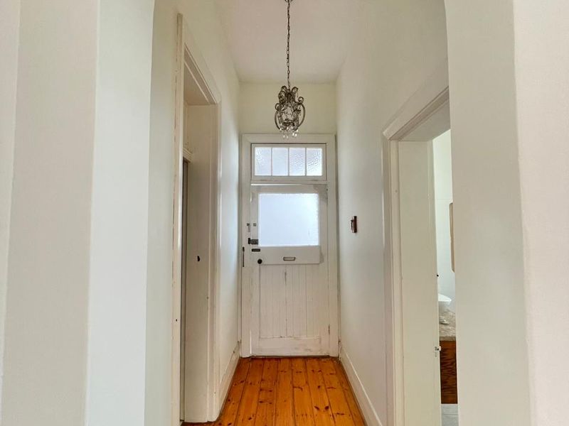 A bright hallway featuring polished timber flooring, an arched entryway, and a classic timber front door with a transom window.