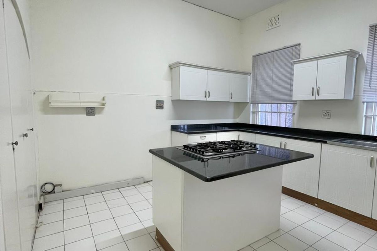 A functional kitchen featuring white cabinetry, granite countertops, a central island with a gas cooktop, and tiled flooring.
