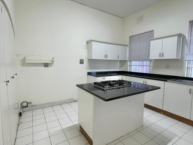 A functional kitchen featuring white cabinetry, granite countertops, a central island with a gas cooktop, and tiled flooring.