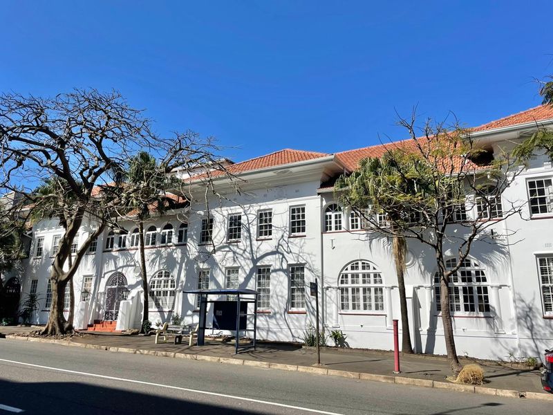 A clear street-level view of the apartment building's historic white facade, featuring classic arched windows and a traditional terracotta tiled roof.
