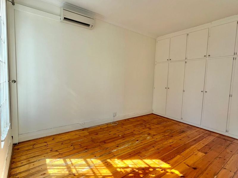 An empty bedroom featuring polished timber flooring, extensive built-in storage cupboards, and a wall-mounted split-system air conditioning unit.