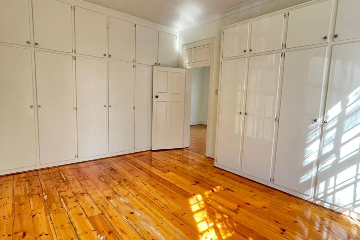 Empty bedroom featuring extensive built-in storage cupboards and original timber flooring with visible signs of wear.