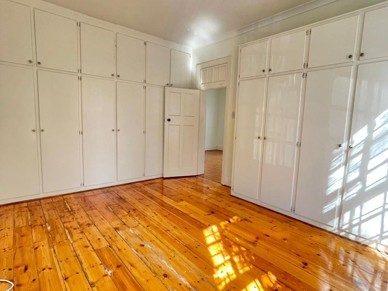 Empty bedroom featuring extensive built-in storage cupboards and original timber flooring with visible signs of wear.