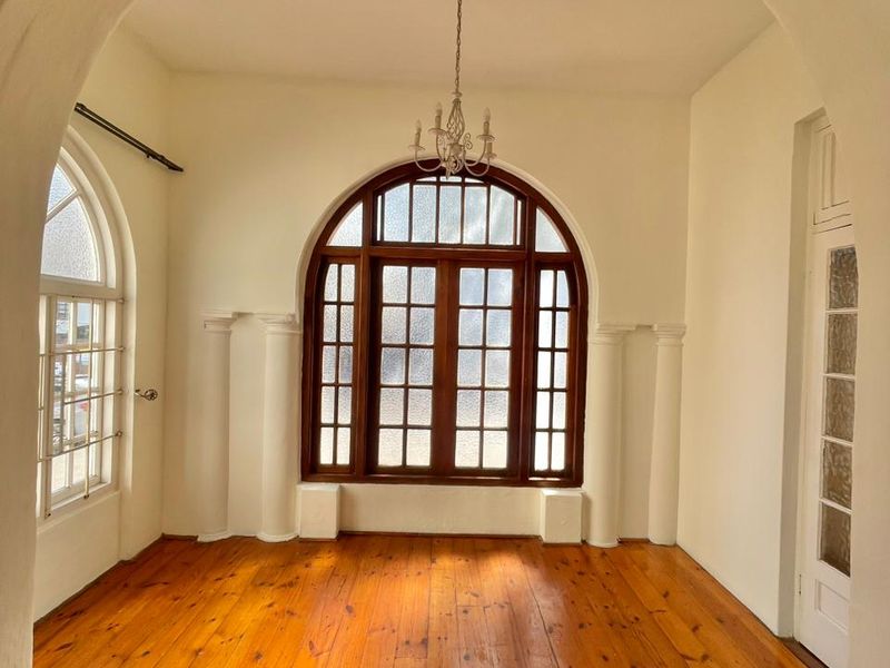 A bright, empty living space featuring polished timber flooring, distinctive arched timber-framed windows, and an elegant arched entryway.