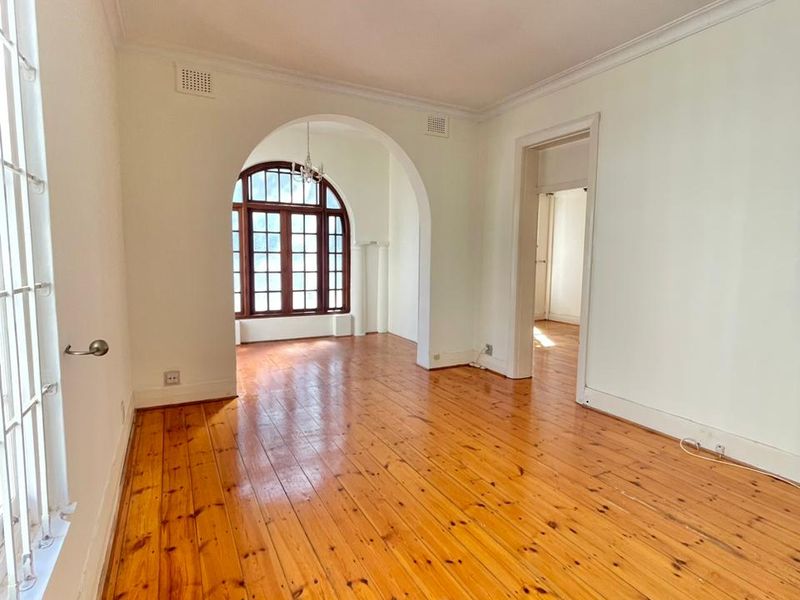 Bright and spacious living area featuring polished timber flooring, an elegant arched doorway, and a large timber-framed arched window providing natural light.