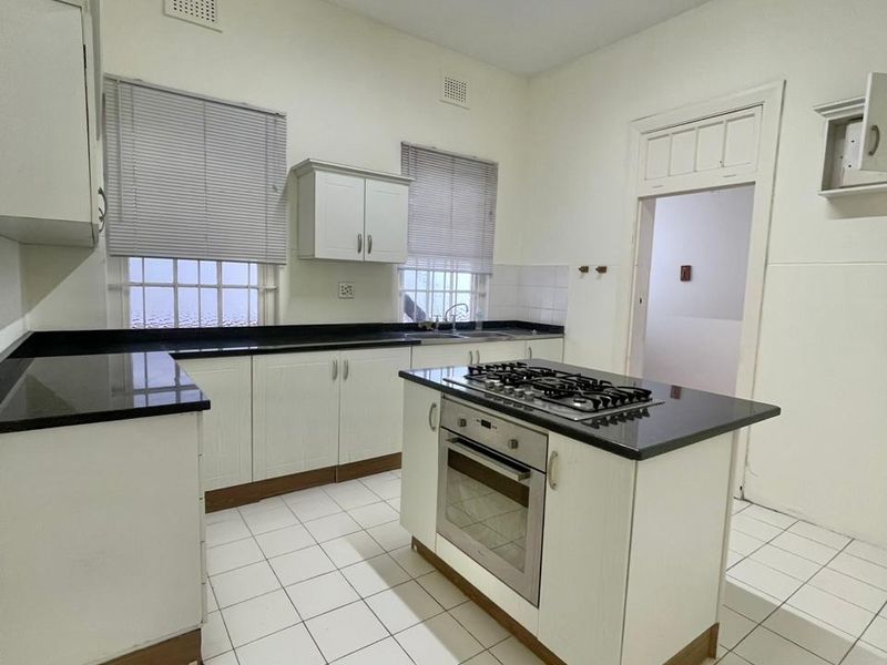 A functional kitchen featuring a central island with a built-in oven and gas cooktop, black granite countertops, and white cabinetry with tiled flooring.