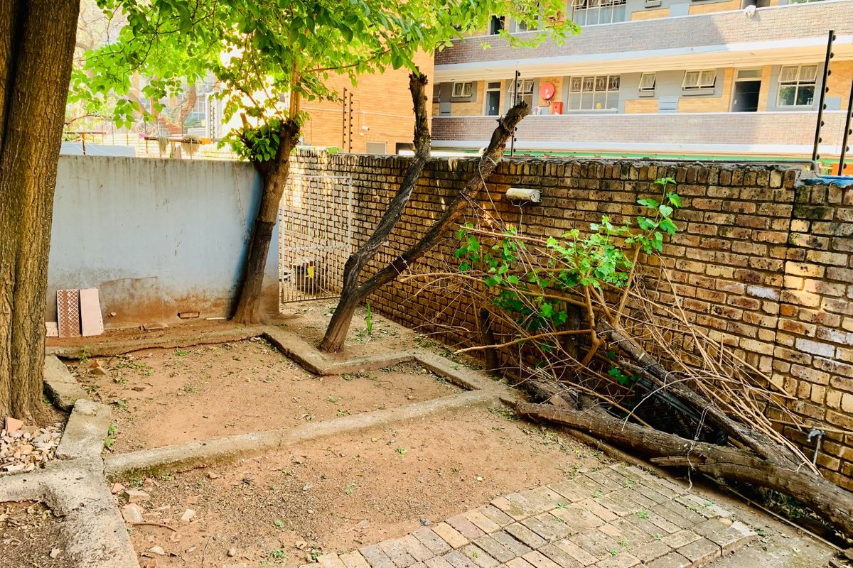 A rear outdoor area featuring a brick boundary wall with electric fencing, paved sections, and significant space for landscaping or garden development.