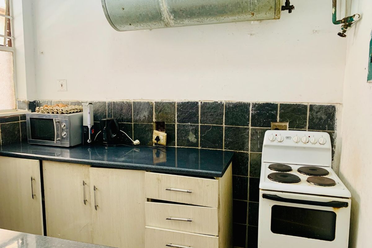 A dated kitchen featuring laminate cabinetry, a tiled backsplash, and an exposed electric water heater above the stove area.