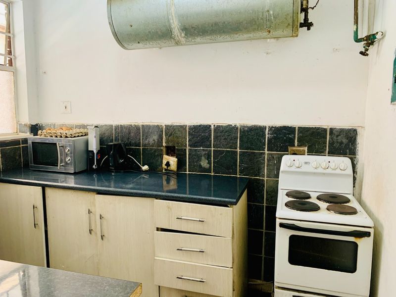 A dated kitchen featuring laminate cabinetry, a tiled backsplash, and an exposed electric water heater above the stove area.
