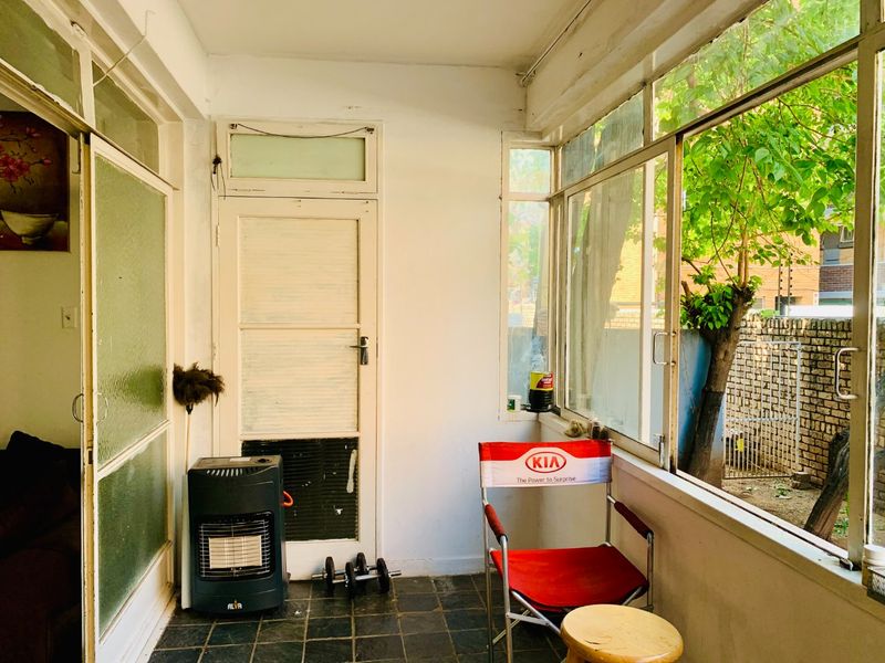 An enclosed balcony area featuring tiled flooring and large windows, providing a bright, versatile space with views of the garden.