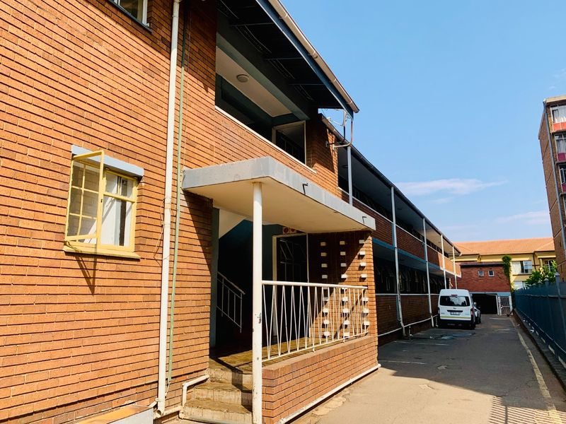 Exterior view of a multi-story brick apartment building featuring a covered entrance, metal railings, and concrete stair access.