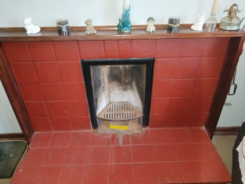 A traditional fireplace featuring a red tiled surround and hearth with a timber mantelpiece, showing signs of age and wear.