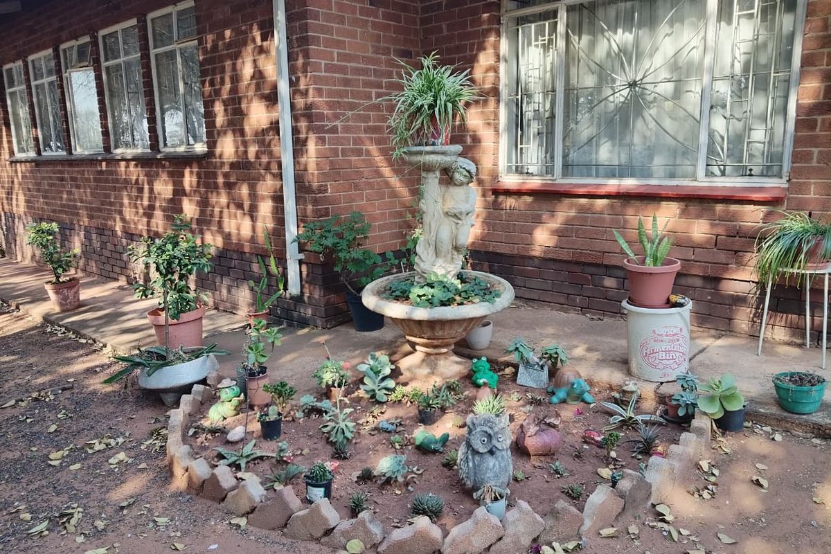 A rear garden area featuring a brick facade, security-barred windows, and a landscaped circular garden bed with a central stone fountain.