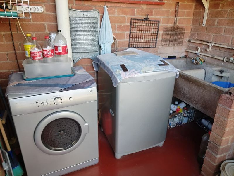 A functional laundry area featuring exposed brick walls, a traditional concrete wash trough, and dedicated space for laundry appliances.