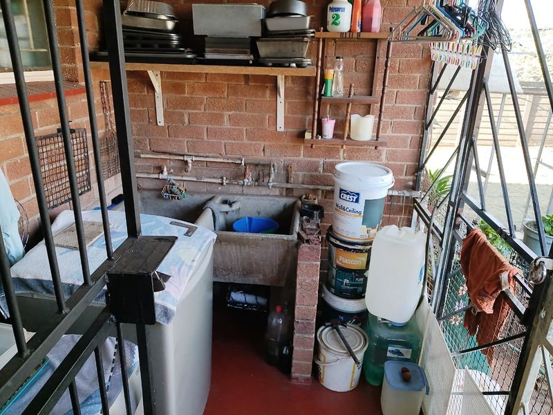 A functional laundry area featuring a traditional concrete sink, exposed brick walls, and wall-mounted shelving, providing a practical utility space.