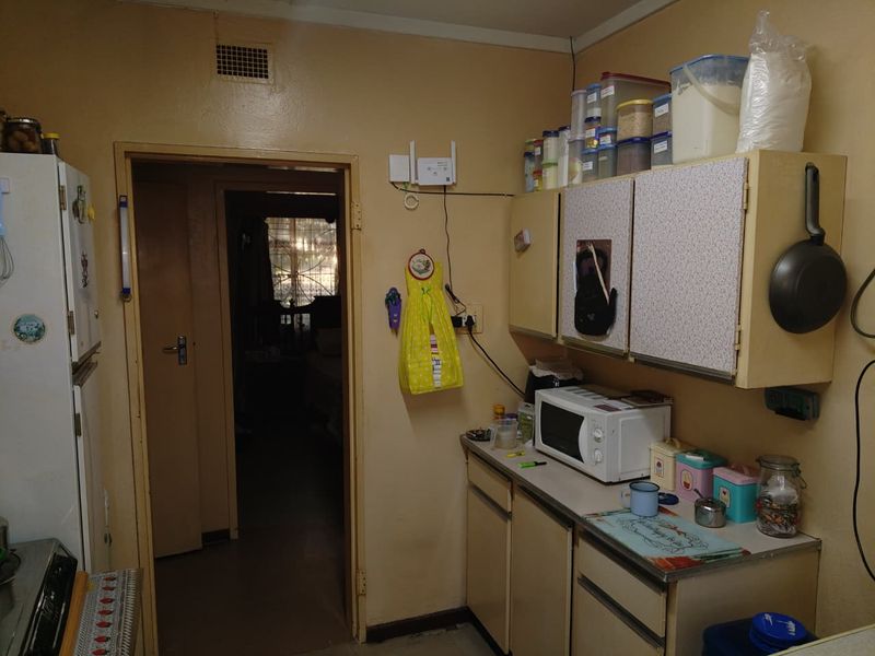 A compact kitchen featuring dated built-in cabinetry and laminate countertops, providing a functional workspace with direct access to the hallway.