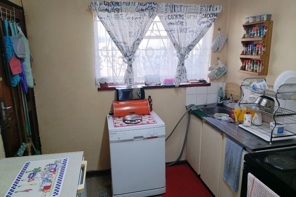 A functional kitchen area featuring basic cabinetry, a stainless steel sink, and security bars on the window, offering potential for modernization and cosmetic updates.