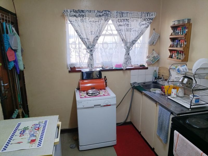 A functional kitchen area featuring basic cabinetry, a stainless steel sink, and security bars on the window, offering potential for modernization and cosmetic updates.