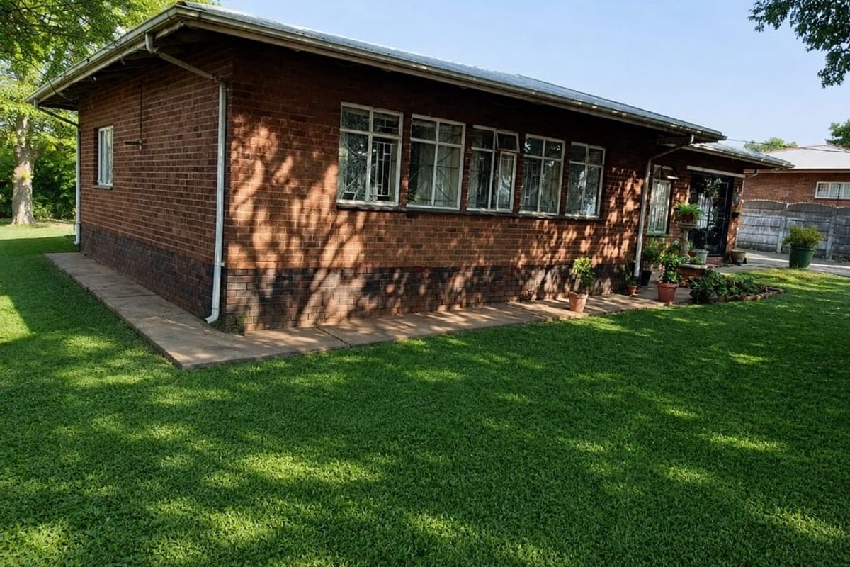 A view of the rear brick exterior of the house, featuring a metal roof, steel-framed windows with security bars, and a surrounding lawn.