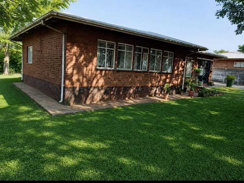 A view of the rear brick exterior of the house, featuring a metal roof, steel-framed windows with security bars, and a surrounding lawn.
