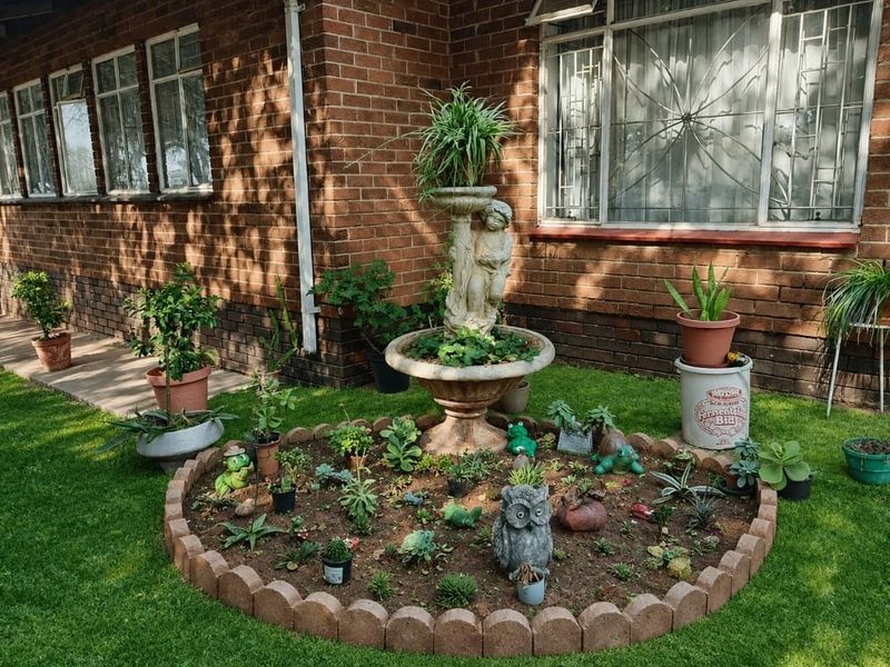 A landscaped garden bed featuring a stone water feature, set against a classic brick exterior wall with security window bars.