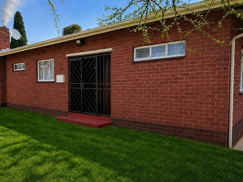 A view of the rear exterior featuring a red brick facade, security gate, and well-maintained lawn.