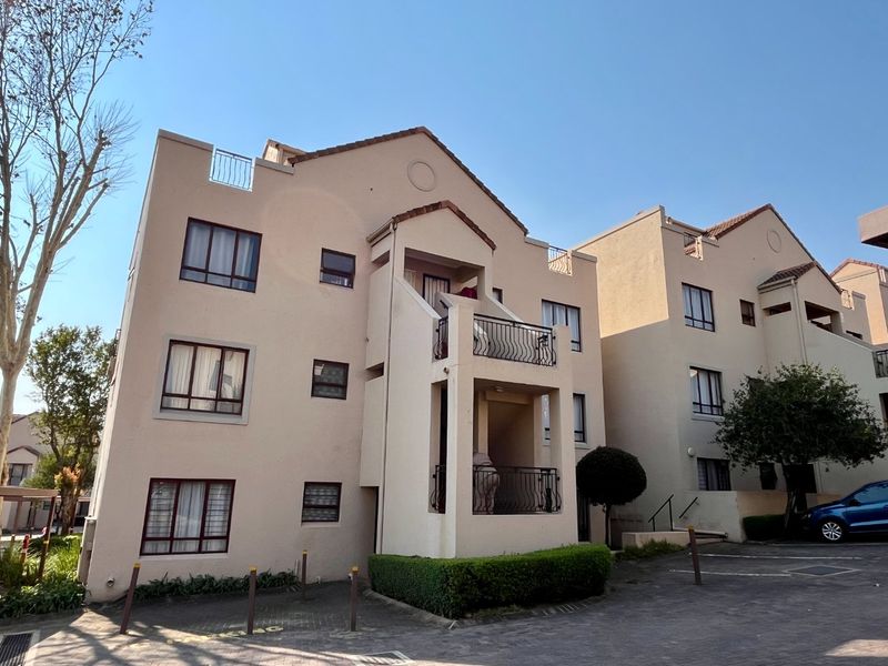 Front elevation of a multi-story townhouse complex featuring balconies with wrought iron railings, tiled roofing, and paved driveway access.