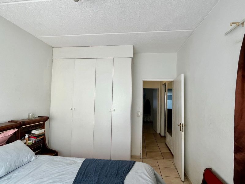 A bedroom featuring built-in wardrobes and tiled flooring, with an open doorway leading to an adjacent hallway.