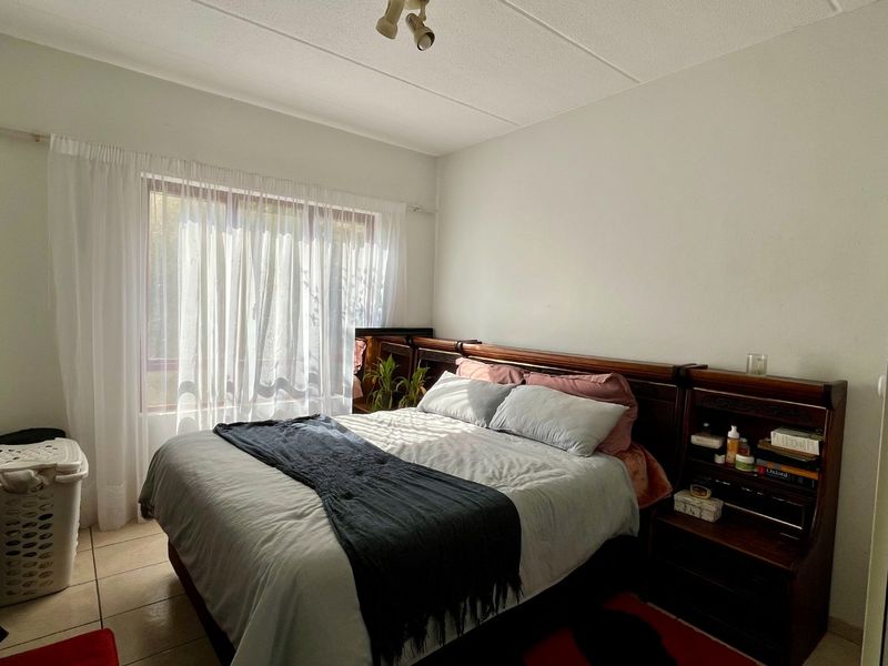 A functional bedroom featuring tiled flooring and a ceiling-mounted spotlight fixture, with natural light entering through a large window.