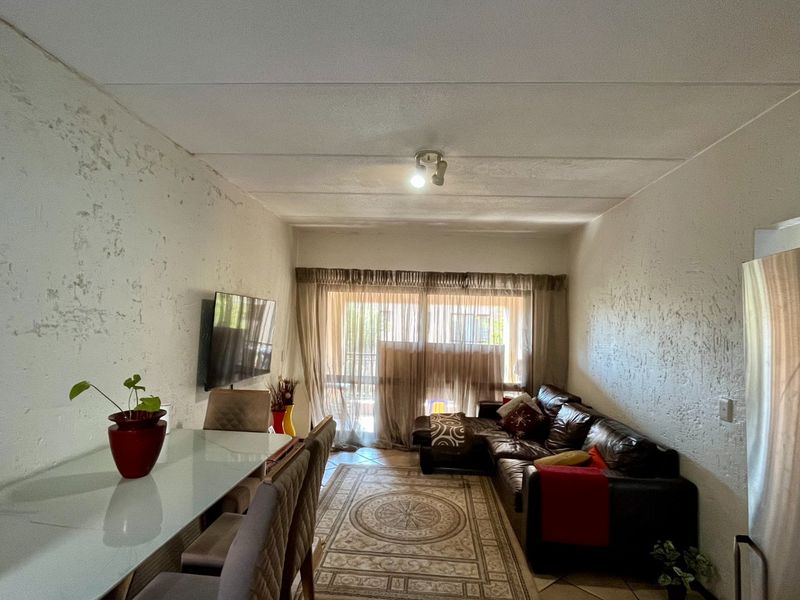 Open-plan living and dining area featuring tiled floors and a sliding glass door leading to an outdoor space, with walls requiring cosmetic attention.