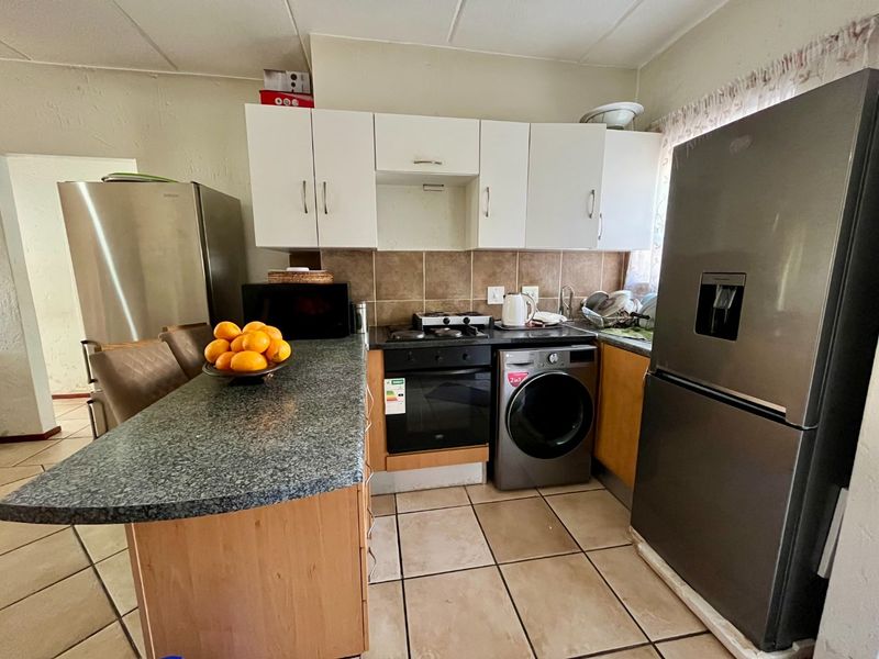 Compact kitchen featuring built-in cabinetry, granite countertops, integrated oven and hob, and tiled flooring with a functional layout.