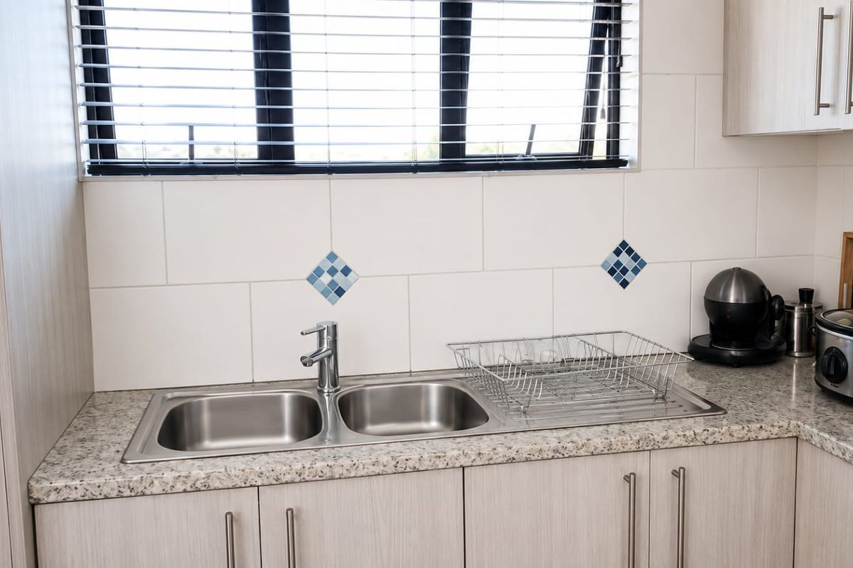 A clean kitchen area featuring a double bowl stainless steel sink, granite countertops, and light wood-tone cabinetry with a tiled backsplash.