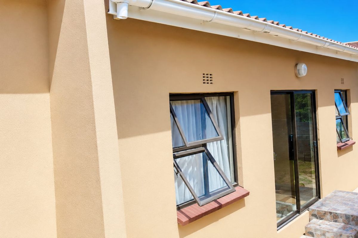 Rear exterior view of the property featuring aluminium window frames, a sliding glass door, and tiled steps leading to the garden area.