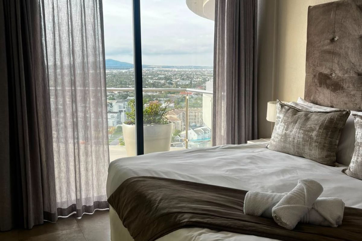A well-maintained bedroom featuring large sliding glass doors that open onto a balcony with expansive city views.