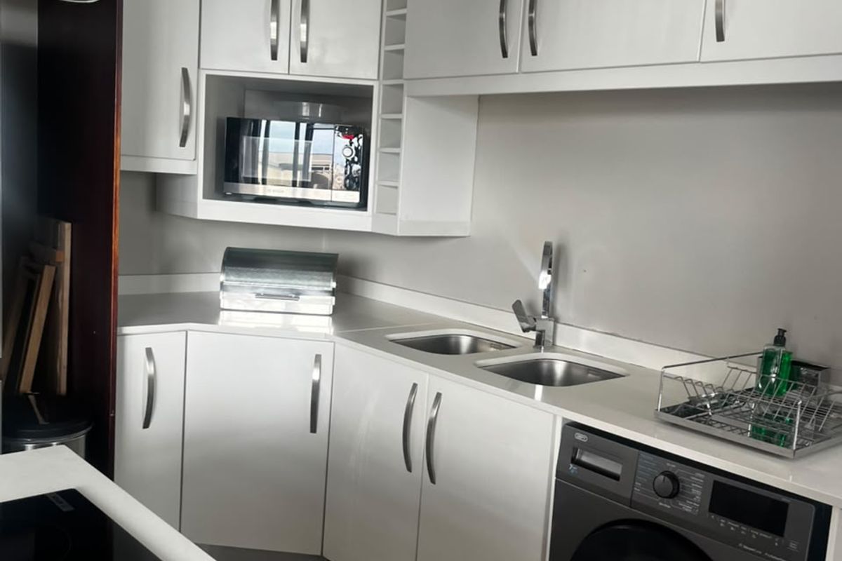 Modern kitchen featuring white cabinetry, integrated washing machine, electric hob, extractor fan, and a double stainless steel sink with a sleek mixer tap.