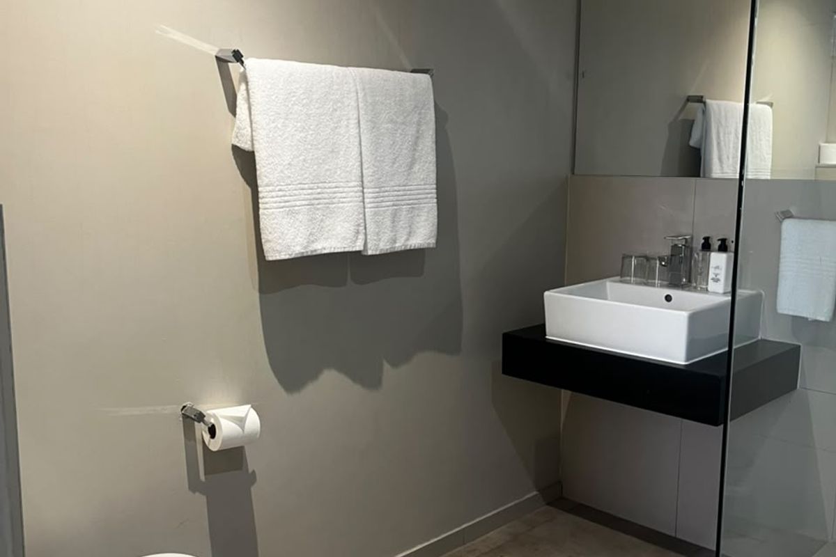 Modern bathroom featuring a floating vanity with vessel sink, wall-mounted toilet, large mirror, and a glass-enclosed shower with neutral tiled flooring.
