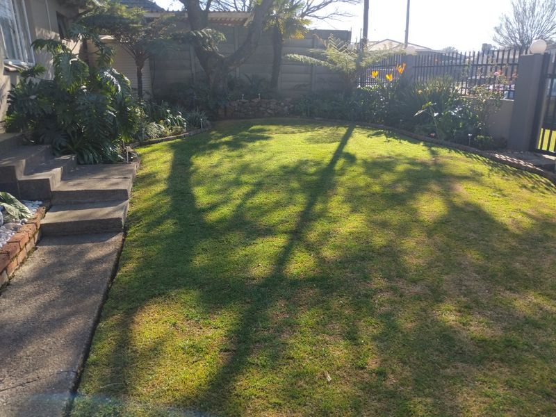 A well-maintained residential garden featuring a manicured lawn, established garden beds, concrete steps, and secure perimeter fencing.