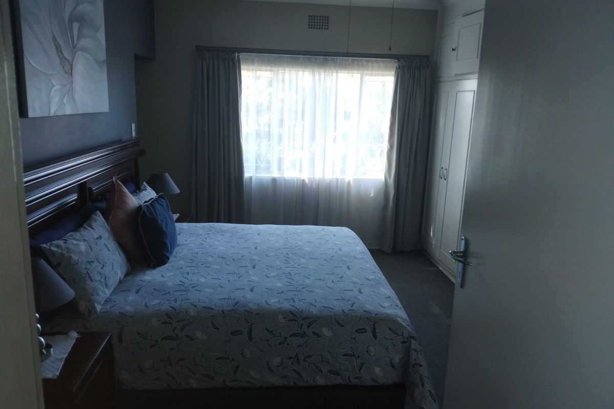 A bedroom featuring built-in cupboards, a ceiling fan, and natural light through a window with curtain rails.