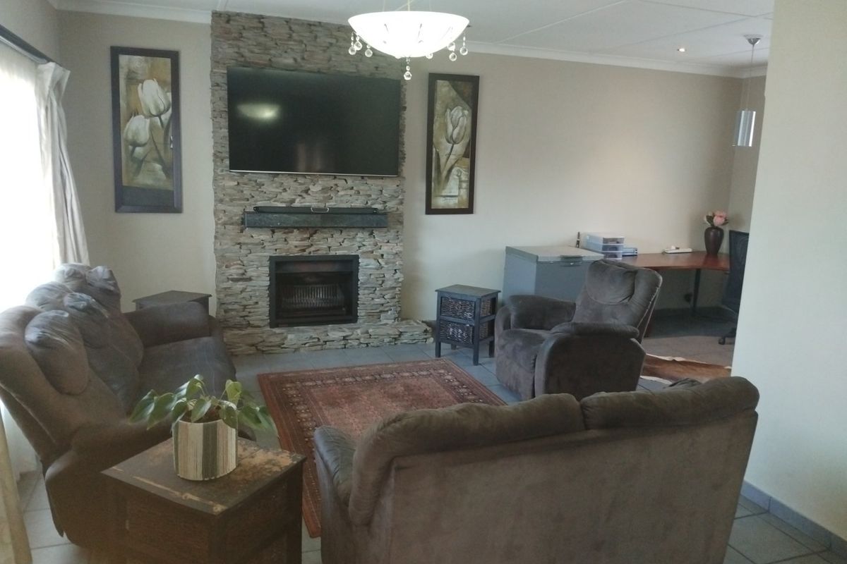 A comfortable living room featuring a prominent stone fireplace, tiled flooring, and recessed lighting, offering a warm and inviting atmosphere.