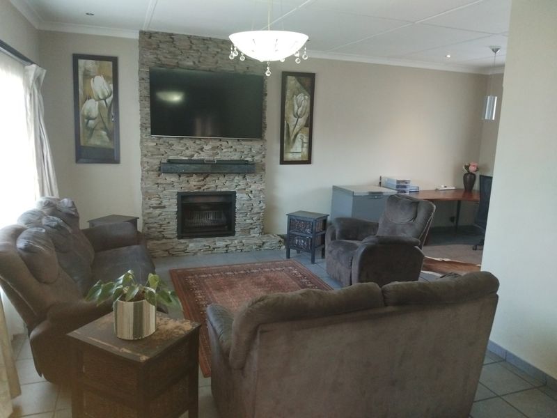 A comfortable living room featuring a prominent stone fireplace, tiled flooring, and recessed lighting, offering a warm and inviting atmosphere.