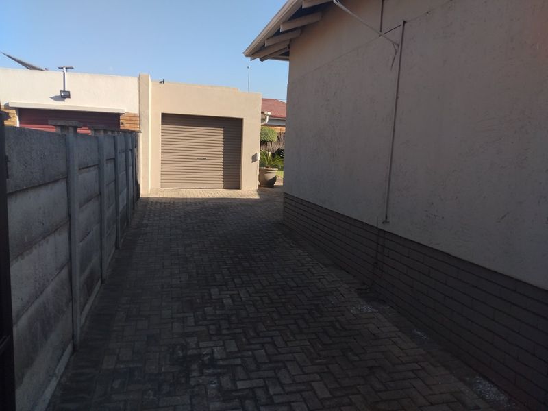 A paved side driveway leading to a single garage, bordered by a precast concrete boundary wall and the side elevation of the main house.