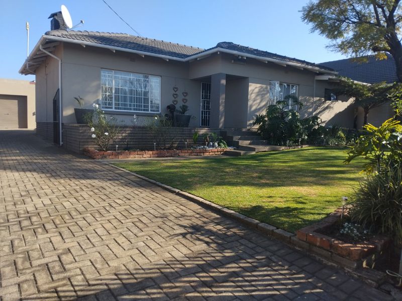 Front view of a well-maintained single-story house featuring a paved driveway, landscaped front garden, and secure window bars.