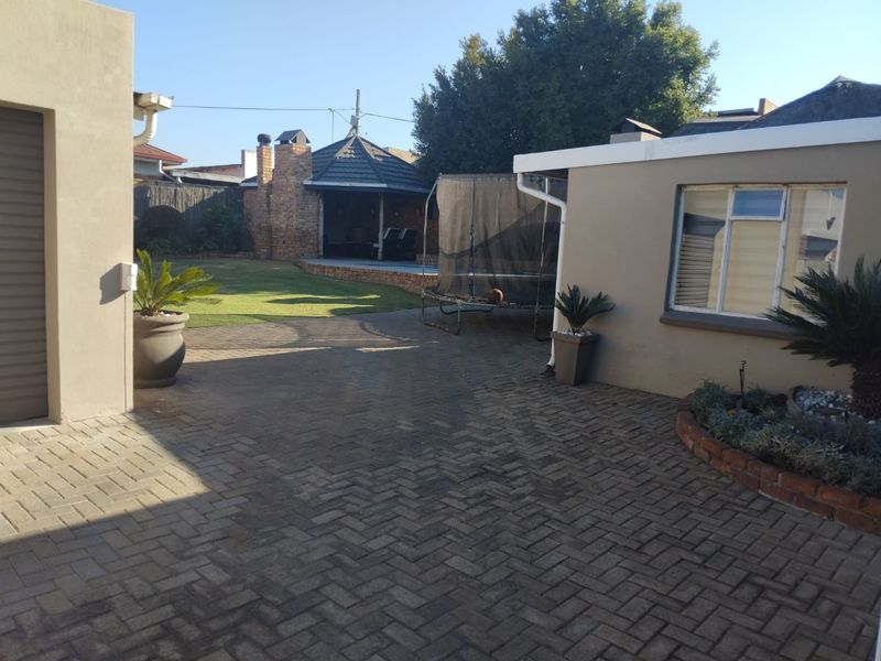 Rear exterior view featuring a paved courtyard, brick gazebo, and established garden area with a brick chimney structure.