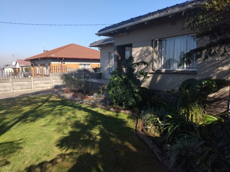 Front view of the house featuring a well-maintained garden, paved driveway, and secure boundary walling in a residential neighborhood.