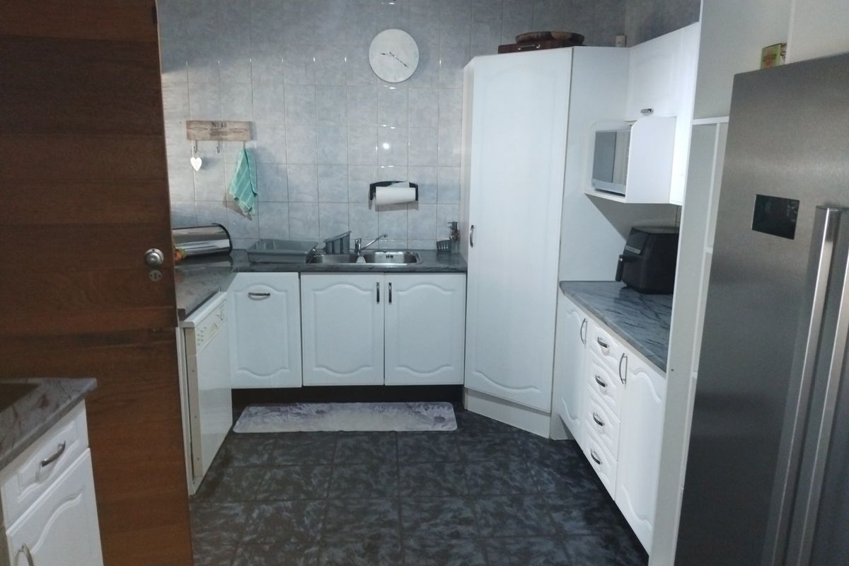A functional kitchen featuring white cabinetry, laminate countertops, a stainless steel sink, and tiled finishes throughout.